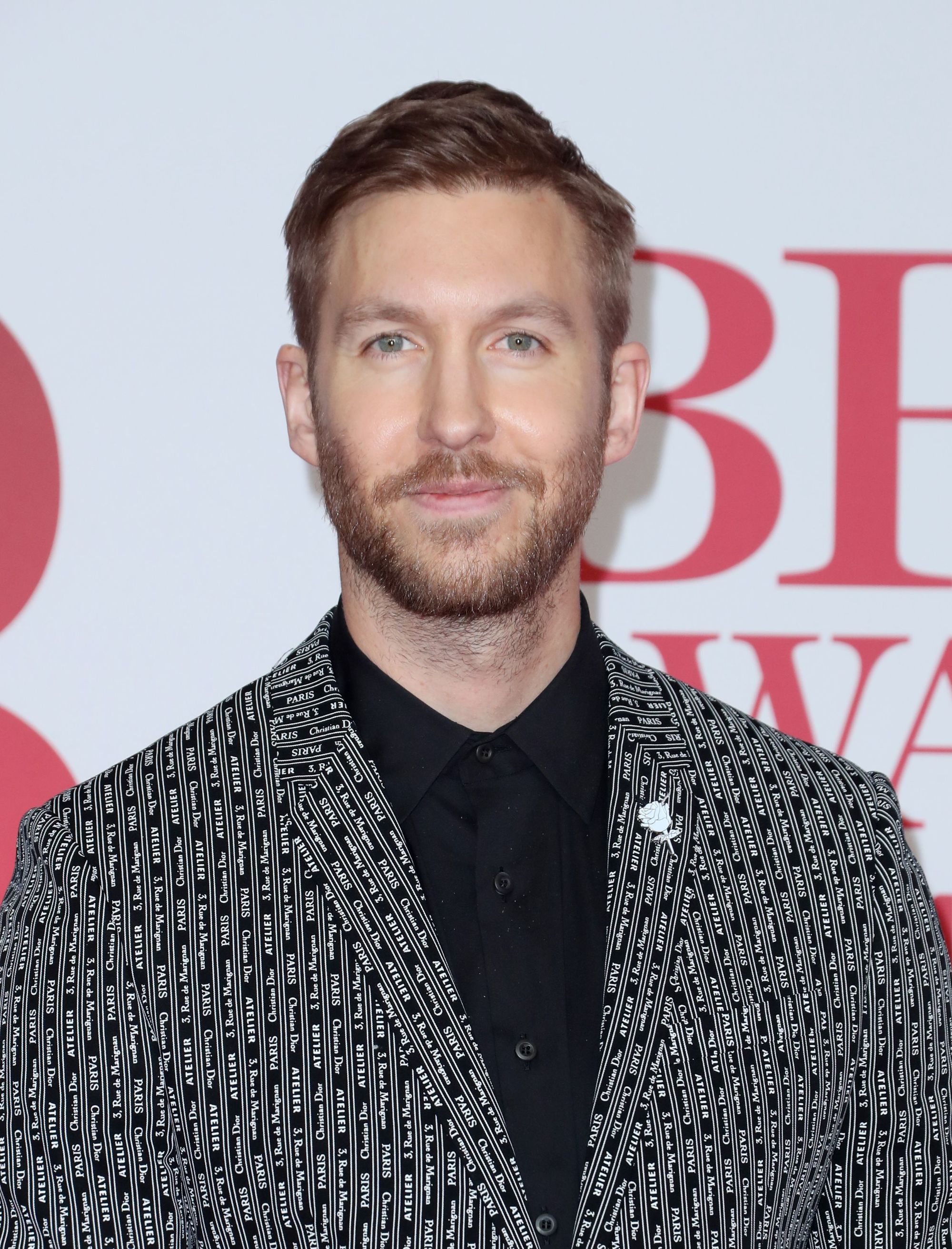 Coupe de cheveux Ivy League: Calvin Harris avec une coupe de cheveux blonde foncée Ivy League, vêtu d'un blazer à motifs et d'une chemise noire