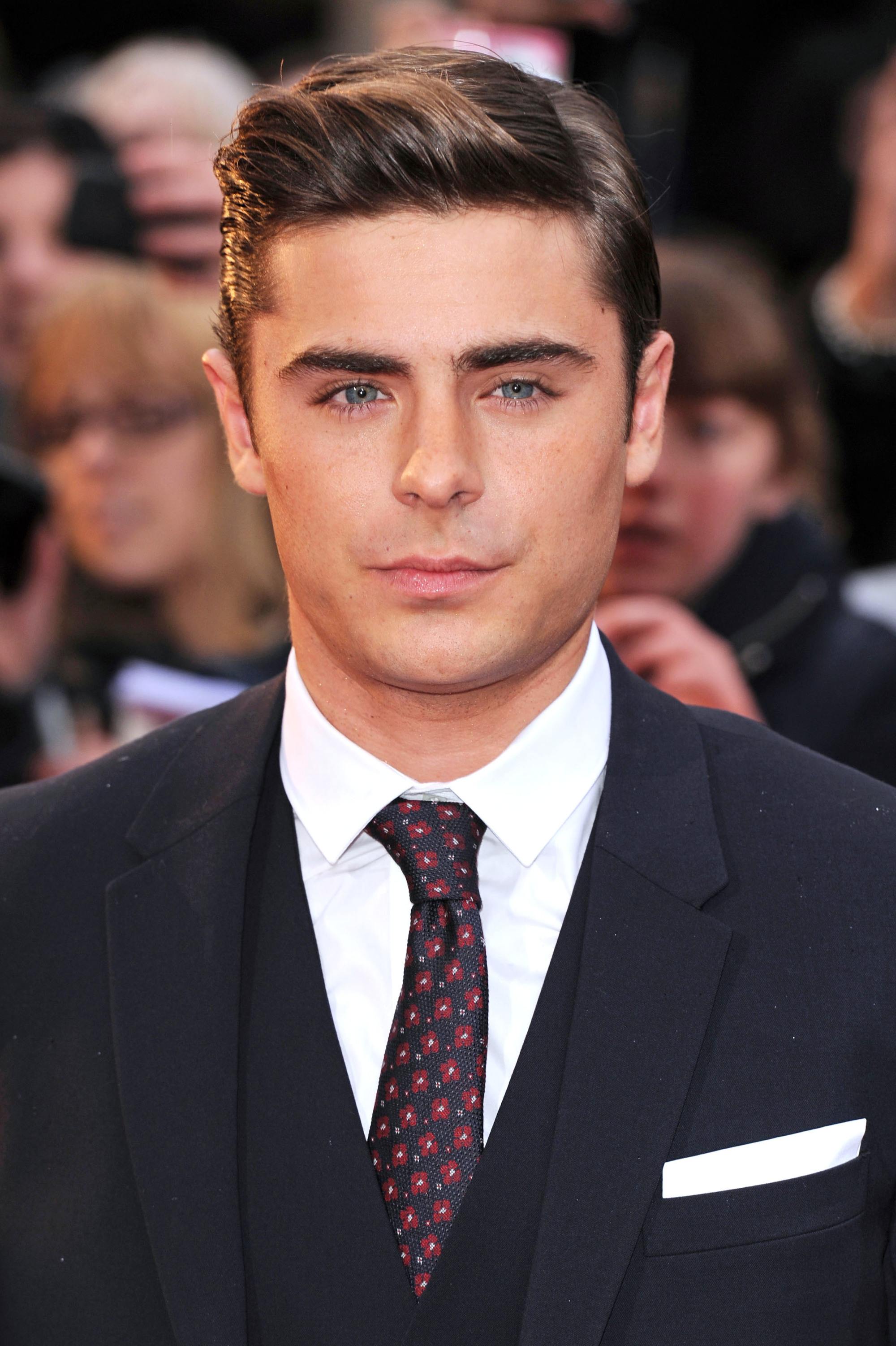Coupe de cheveux Ivy League: Zac Efron aux cheveux bruns dans une longue coupe de cheveux Ivy League, sur le tapis rouge en costume et cravate