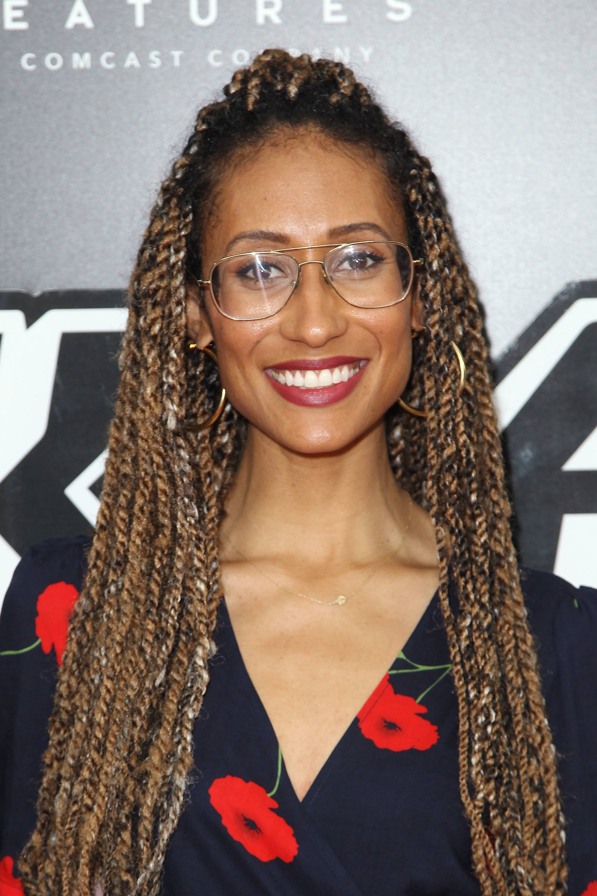 Elaine Welteroth with long caramel marley twists, wearing glasses with print black top with roses on the red carpet