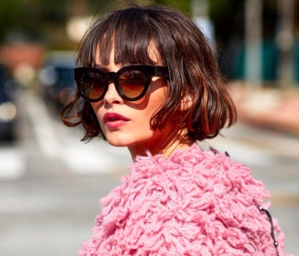 Layered bob: Photo of model/influencer Taylor Lashae with a brunette wavy bob with a fringe, wearing sunglasses and a shaggy pink jacket