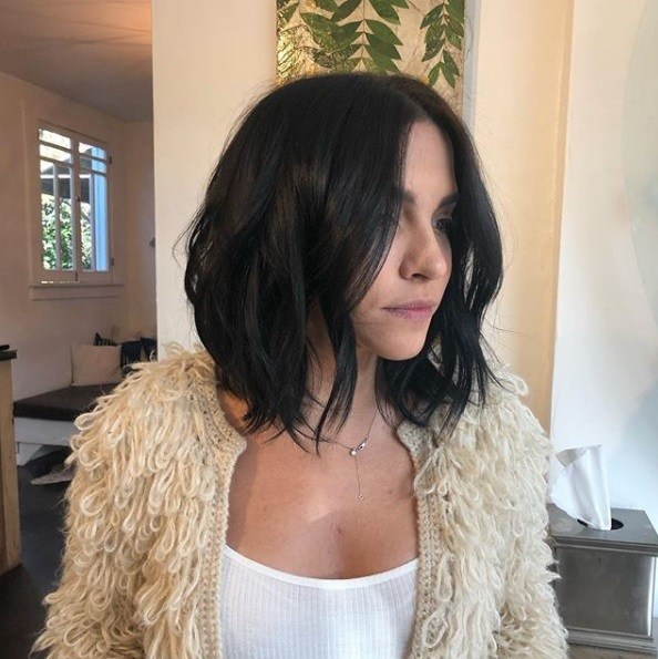 Layered bob: Dark haired woman with a long wavy layered bob, wearing a shaggy beige cardigan