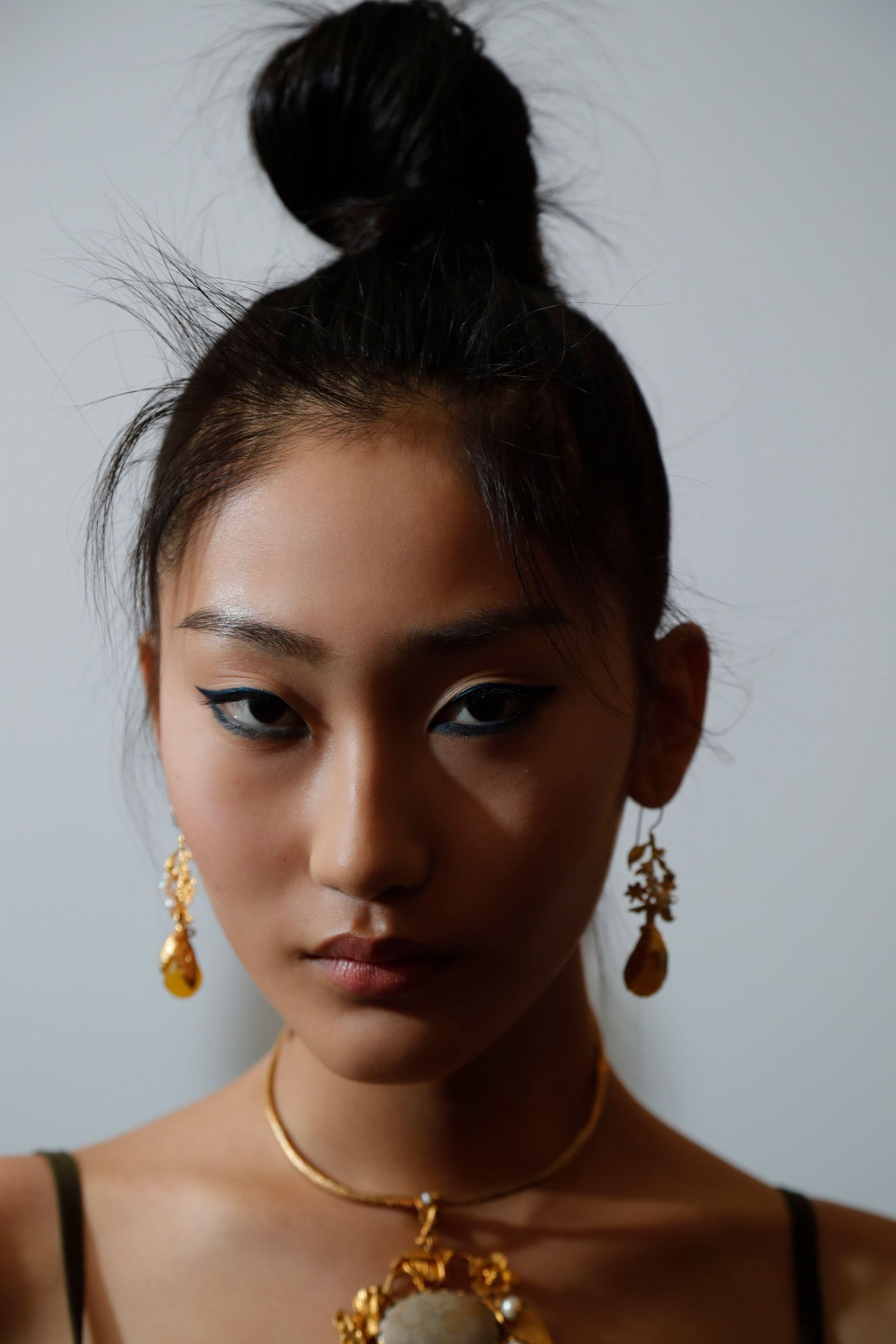 Coiffures faciles pour les cheveux longs: Femme aux cheveux raides brun foncé dans un chignon haut avec des boucles d'oreilles pendantes.