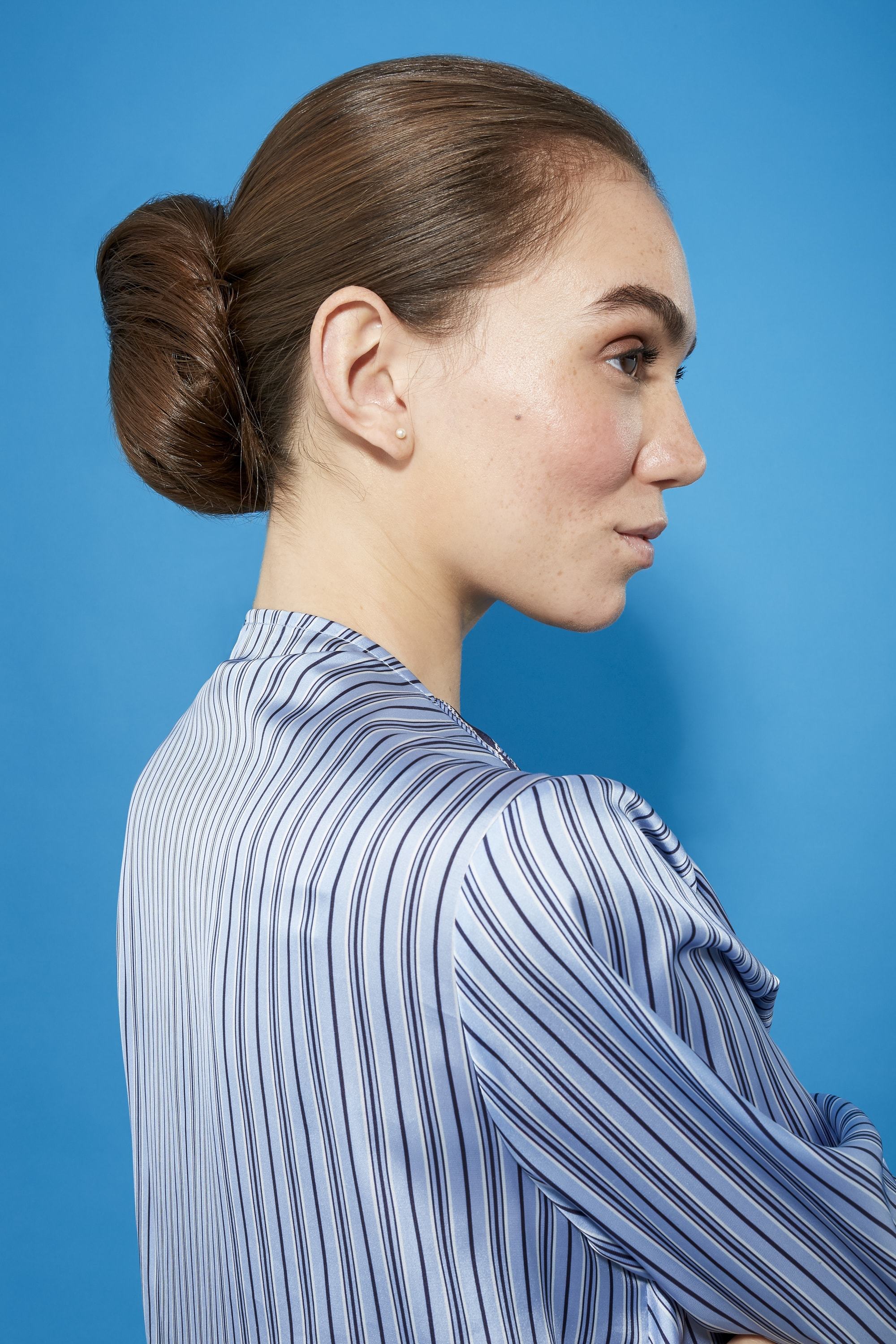 Coiffures faciles pour cheveux longs: Femme aux longs cheveux bruns droits dans un chignon bas en forme de beignet vêtue d'une chemise bleue à rayures.