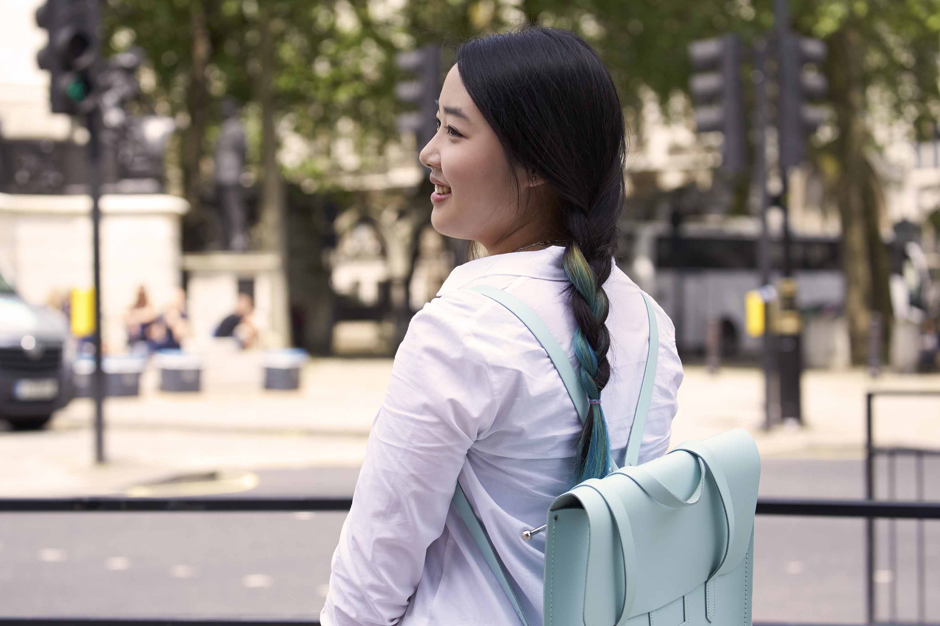Coiffures faciles pour cheveux longs: femme aux longs cheveux bruns foncés avec des reflets bleus coiffés d'une tresse portant un sac à dos bleu clair.