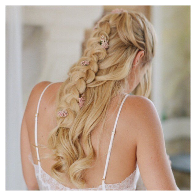 Wedding hairstyles: Woman with golden blonde long hair styled into a half-up, half-down braid with flowers in it, wearing a white wedding dress