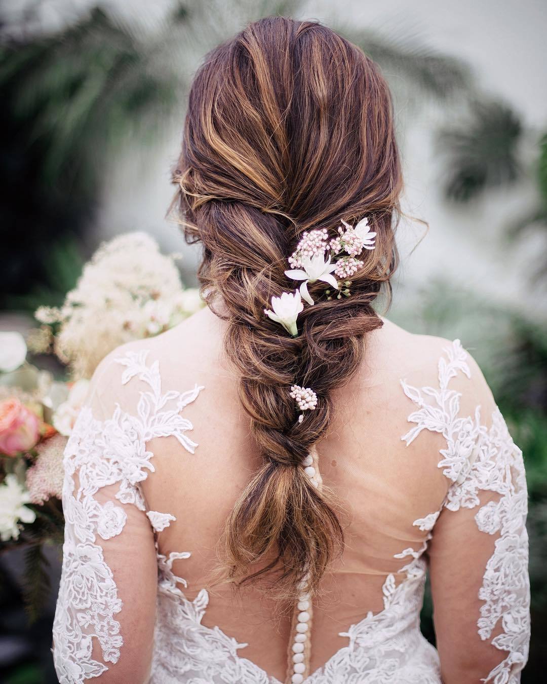 Wedding hairstyles: Woman with long chestnut hair styled into a loose braid with flowers in it, wearing wedding dress and posing outside