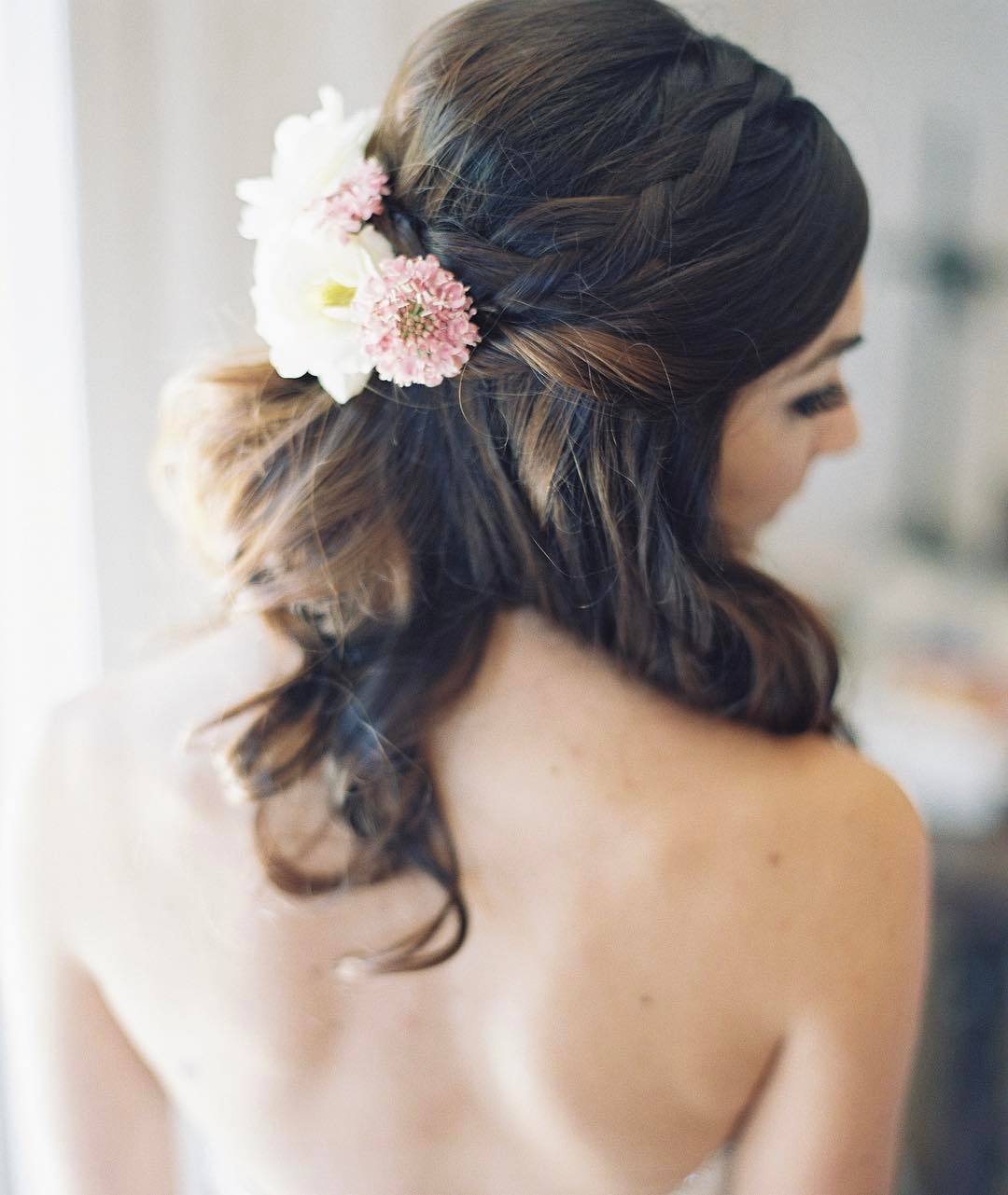 Wedding hairstyles: Woman medium-length dark brown hair styled into a wavy half-up, half-up braids with flowers