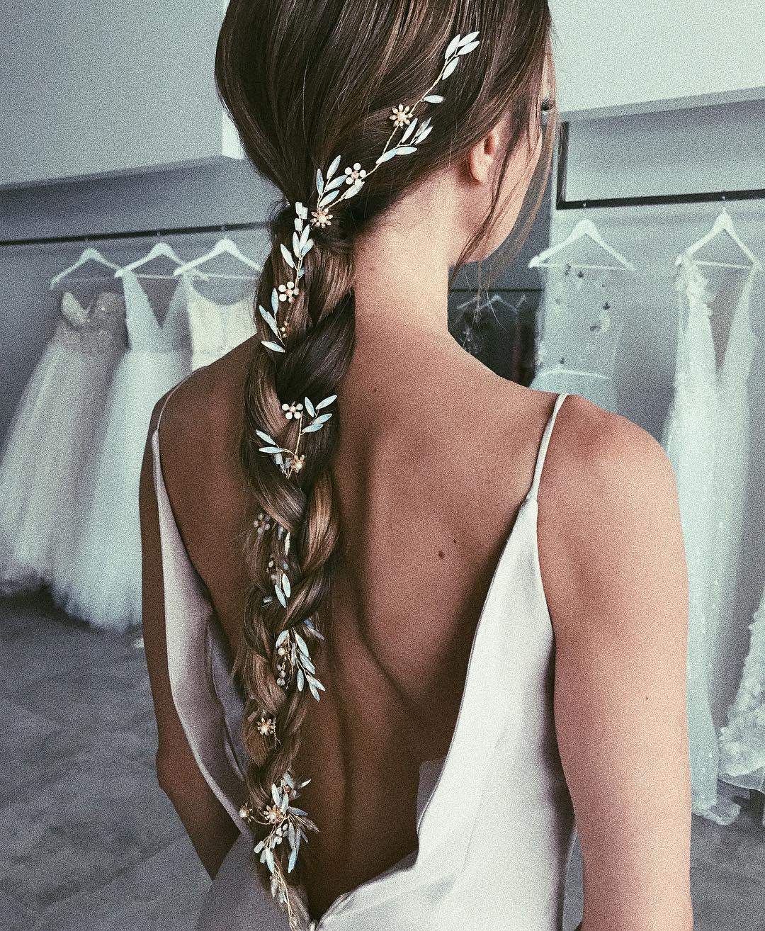 Wedding hair ideas: Shot of woman with dark brown long braided plait with flowers in it, wearing a wedding dress in bridal showroom