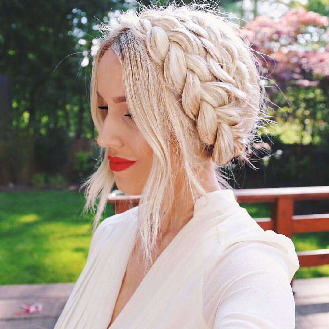 Wedding hairstyles: Woman with milkmaid braid with loose tendrils at the front, wearing a white wedding suit while posing outside
