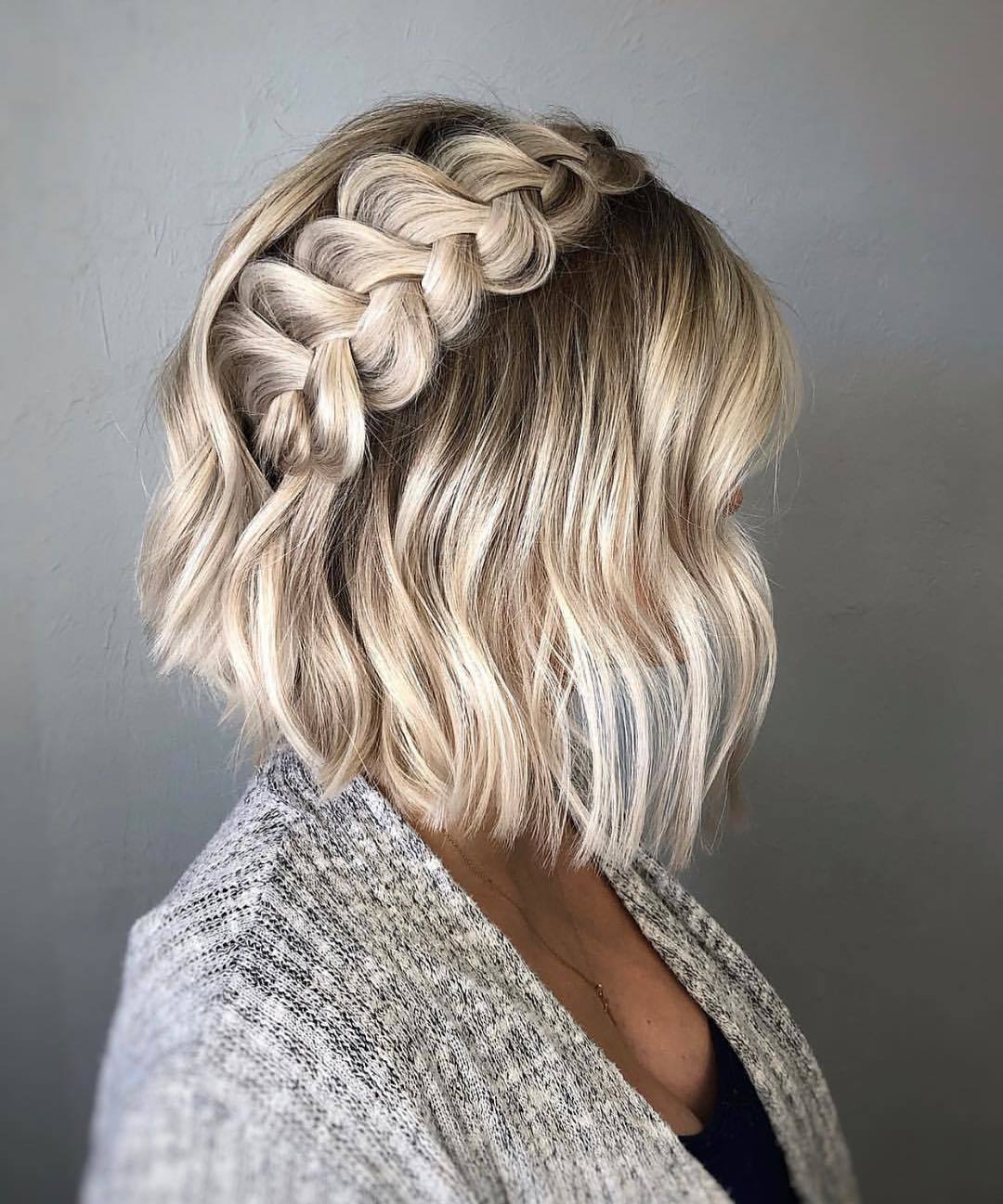 Short wedding hair ideas: Woman with short wavy bronde bob styled into a pinned Dutch braid, posing in a studio