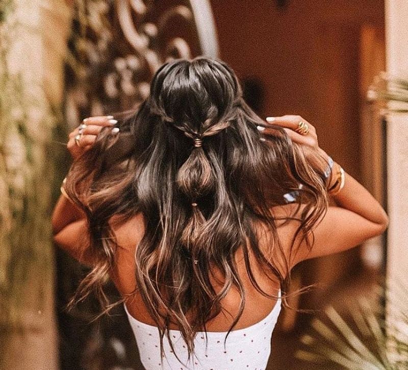 Wedding hairstyles: Woman with chocolate brown hair styled into a half-up, half-down bubble ponytail, wearing white top and posing outside