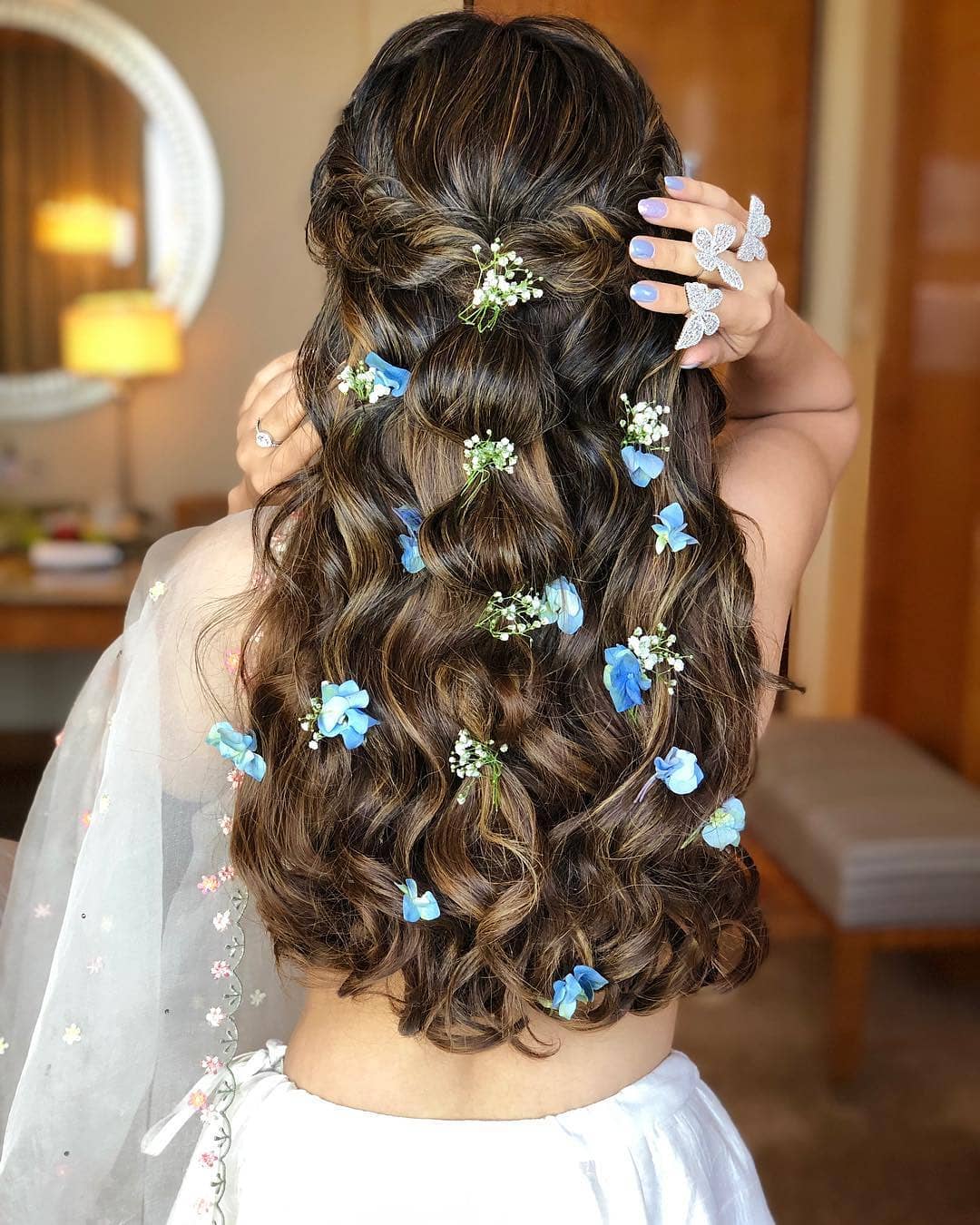 Indian wedding hairstyles: Woman with long flowing dark brown and highlighted hair styled into a half-up bubble with flowers in it
