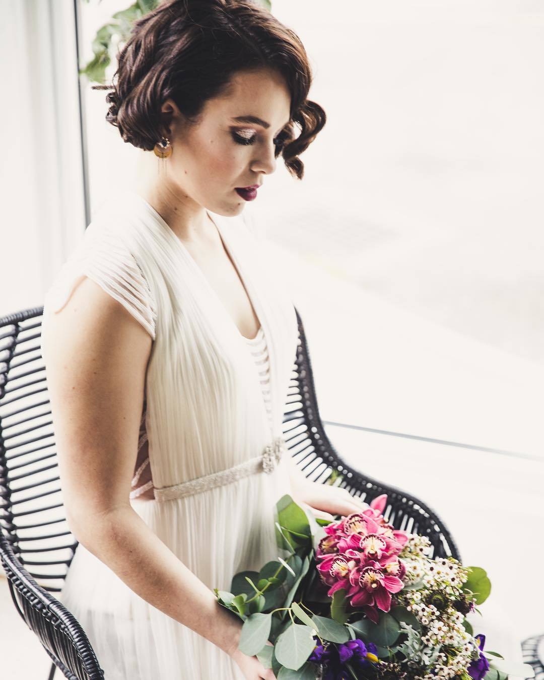 Vintage wedding hairstyles: Woman with short hair styled into retro curls, wearing a dress and holding flowers