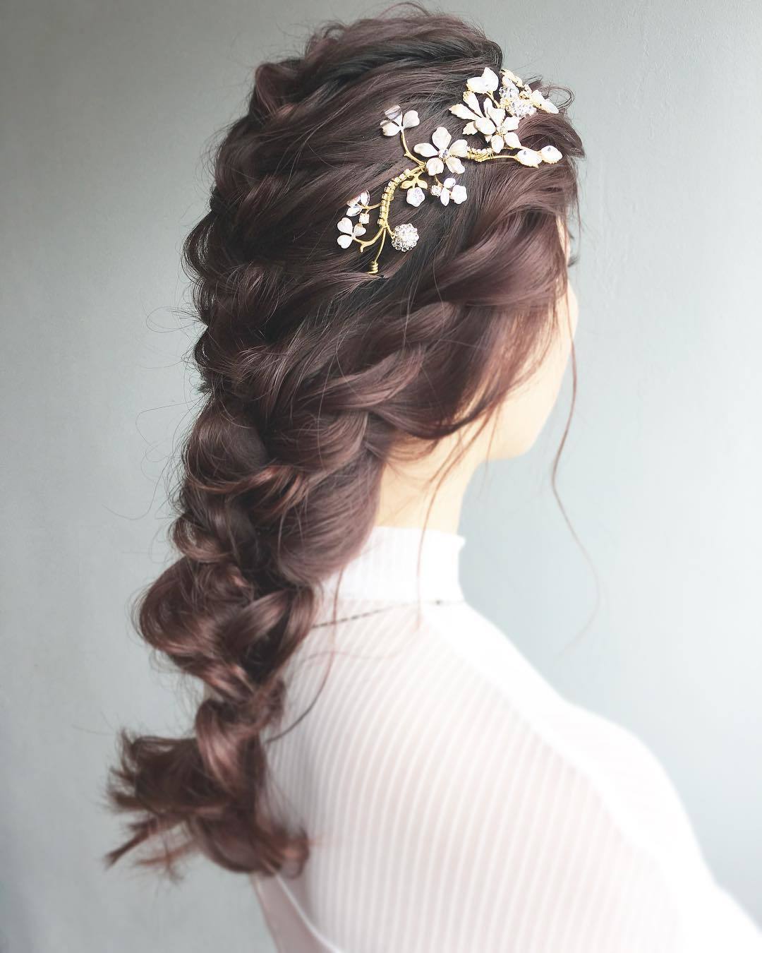Bridal hairstyles: Woman with long mahogany coloured loose French braid with side flowers in it posing in a studio