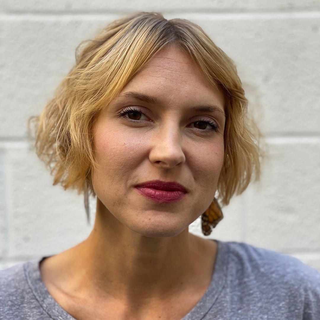 Woman with think golden blonde short hair cut into a very short bob with middle part bangs