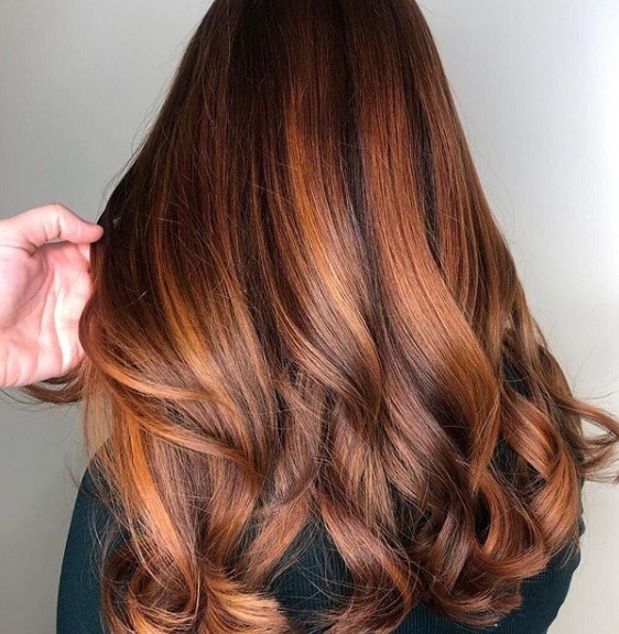 Faits saillants en cuivre: vue arrière d'une femme avec de longs cheveux de balayage en cuivre, coiffés de boucles douces