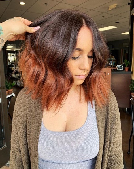 Faits saillants cuivrés: photo d'une femme avec un bob ombré ondulé brun à cuivre, vêtue d'un haut gris et d'un cardigan kaki