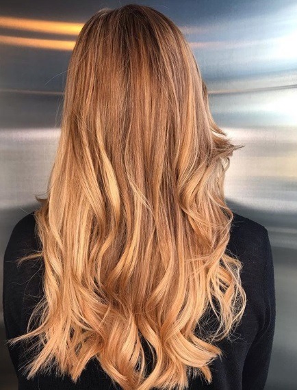 Faits saillants cuivrés: Vue arrière d'une femme aux longs cheveux ondulés blonds fraise avec des reflets