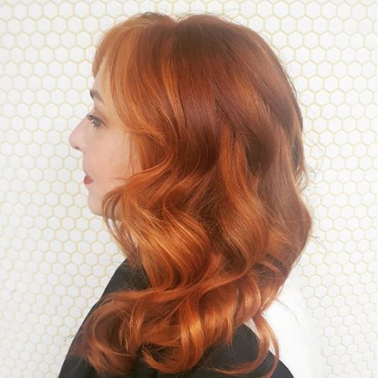 Faits saillants en cuivre: vue de côté d'une femme avec des cheveux ondulés de longueur moyenne en surbrillance de cuivre portant un haut foncé