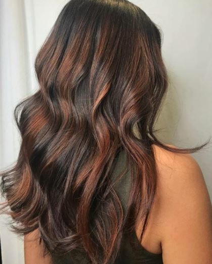 Faits saillants en cuivre: vue arrière d'une femme aux longs cheveux bruns ondulés avec des reflets cuivrés portant un gilet noir