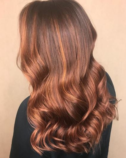 Faits saillants en cuivre: vue arrière d'une femme avec des reflets en or rose et en cuivre sur de longs cheveux ondulés portant un haut noir