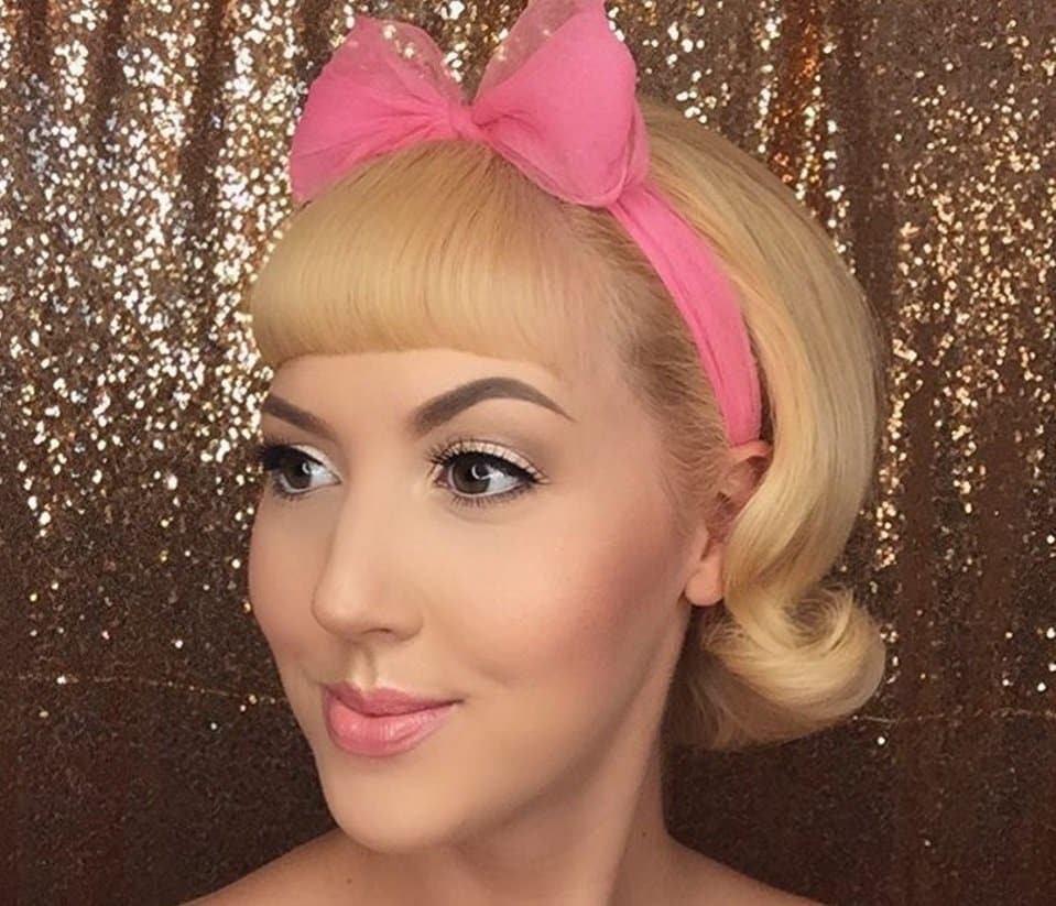femme aux cheveux blonds courts dans un style bob rockabilly et une frange portant un nœud de cheveux roses