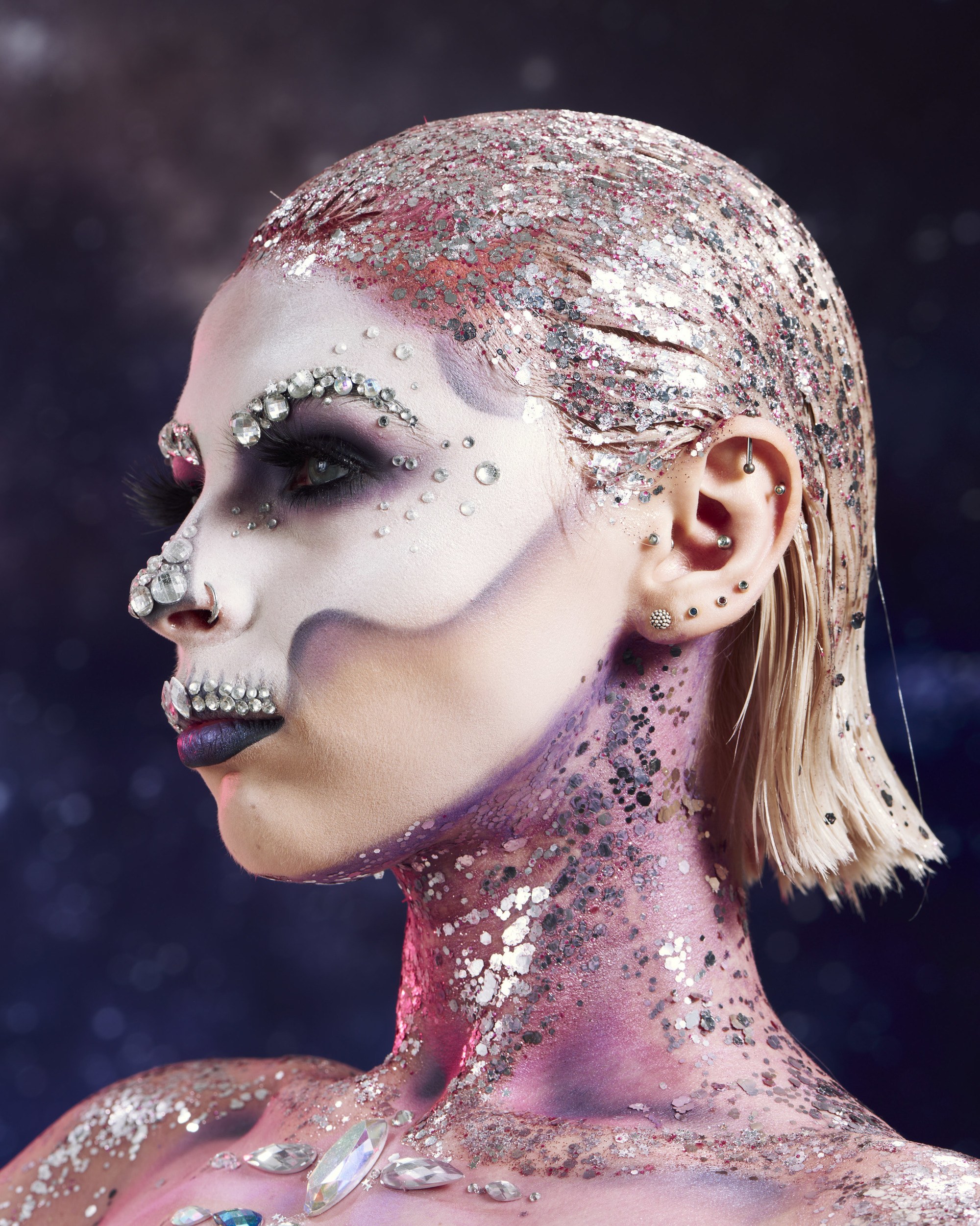 Coiffures d'Halloween : Femme maquillée avec un crâne en sucre, avec des cheveux blonds courts et des paillettes argentées dans le dos, ainsi que sur le cou, posant dans un studio