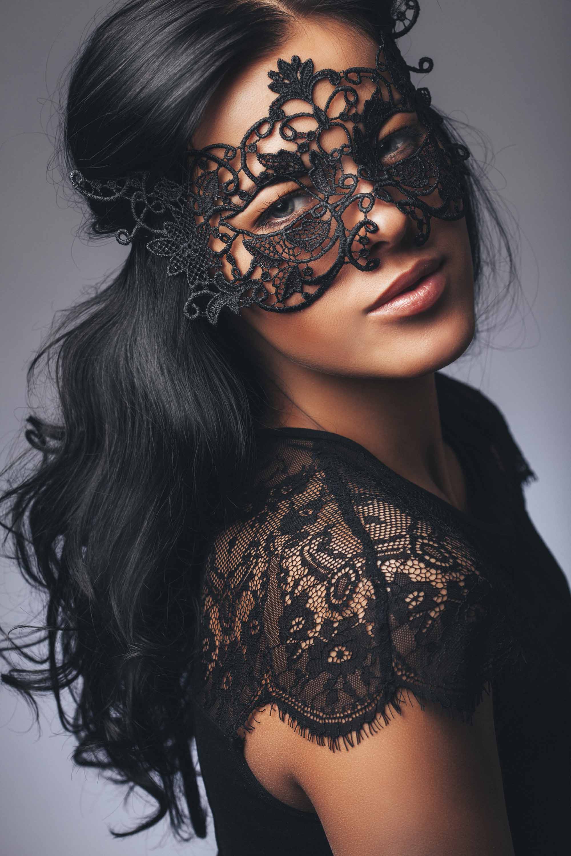 Coiffures d'Halloween : Femme aux longs cheveux noirs en vagues portant un masque de mascarade et un haut en dentelle noire