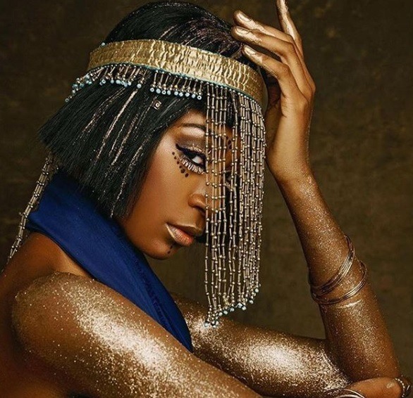 Coiffures noires d'Halloween : Femme habillée en Cléopâtre avec une courte coiffure noire en bob, portant une coiffe dorée avec une robe en soie bleue à paillettes dorées sur le corps