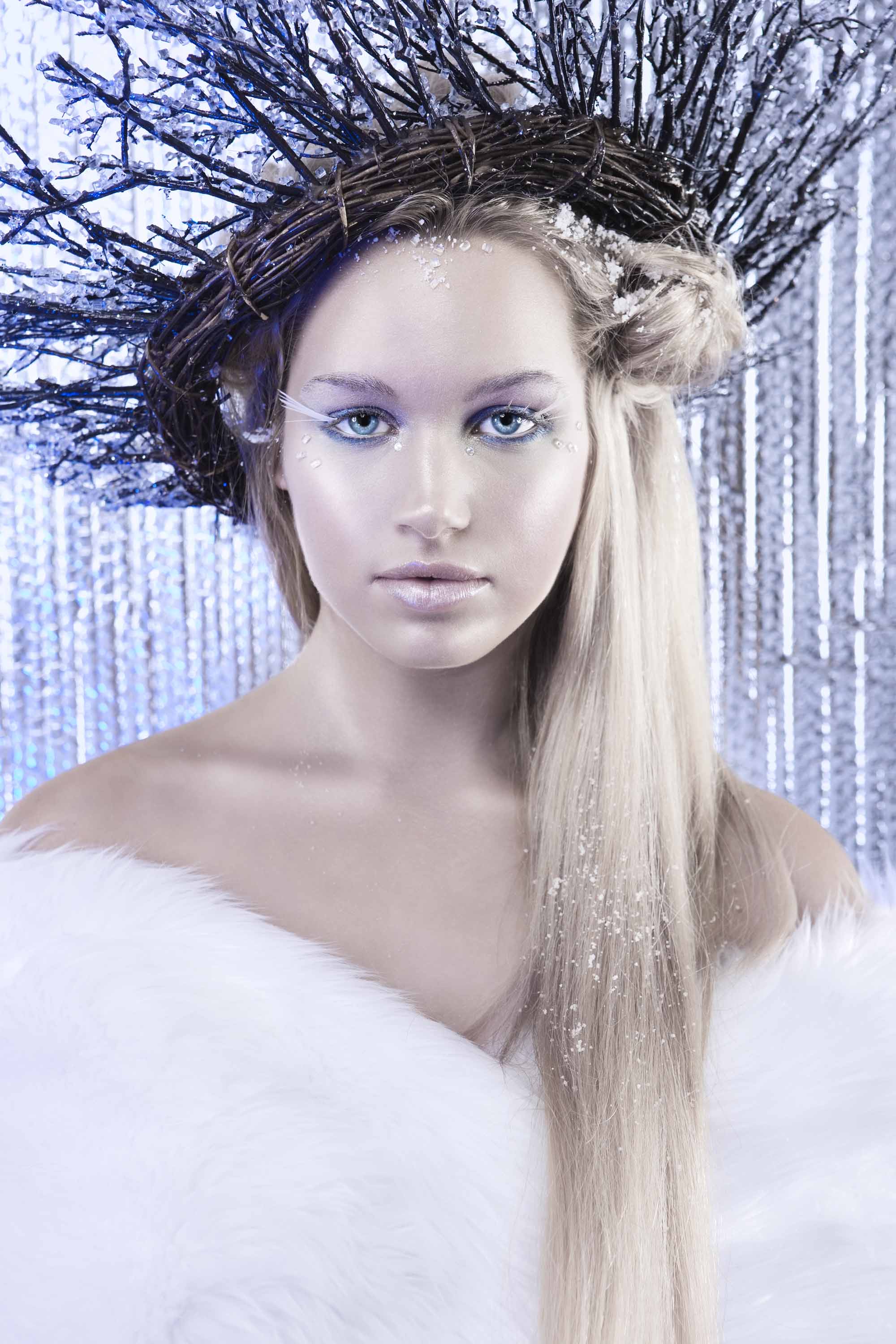 Coiffures d'Halloween : Femme habillée comme une reine de glace avec de longs cheveux blonds, portant une fourrure blanche et des brindilles dans ses cheveux