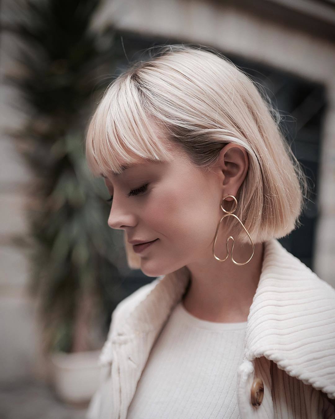 Femme au bob blond court et droit avec une frange de plumes