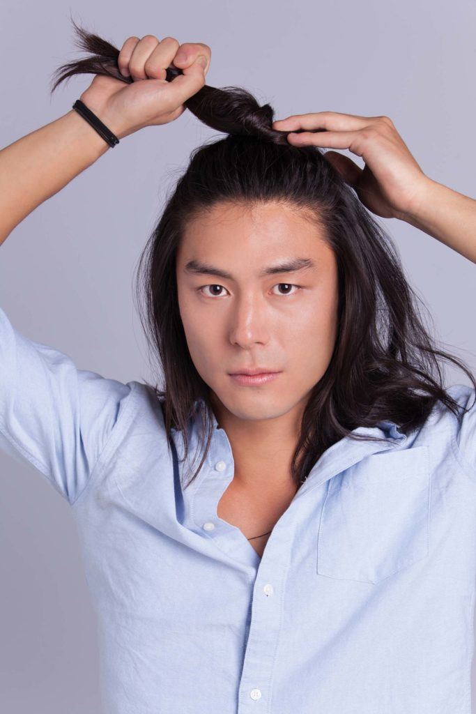 Un homme asiatique, un petit pain : Modèle masculin asiatique aux cheveux longs aux épaules, se tordant les cheveux en un chignon d'homme à moitié relevé