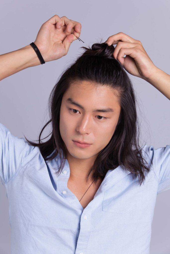 Un homme asiatique, un petit pain : Modèle masculin asiatique aux cheveux longs aux épaules, fixant un chignon d'homme à moitié relevé