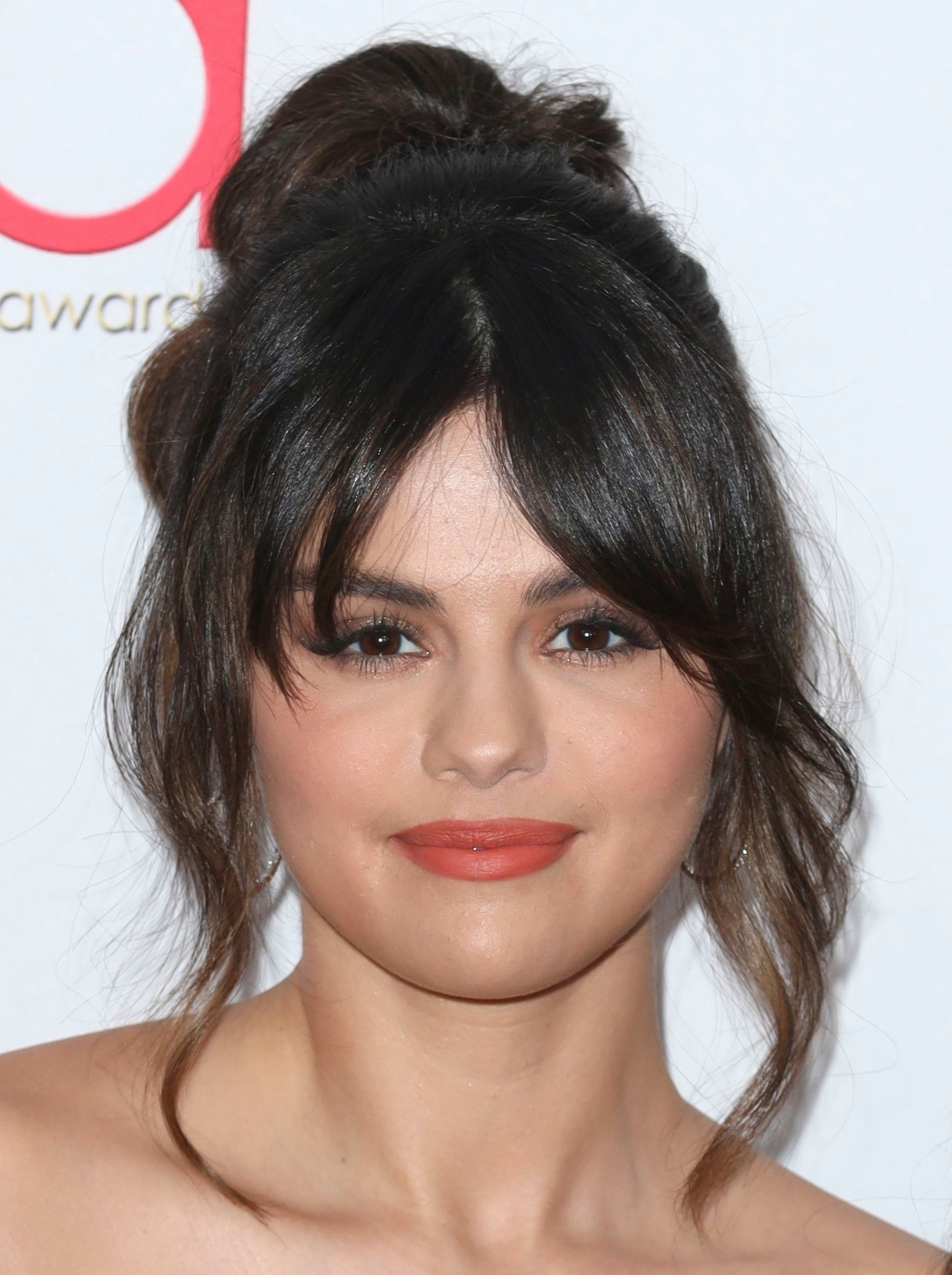 Selena Gomez avec des cheveux bruns dans un updo avec une frange fendue bouclée.