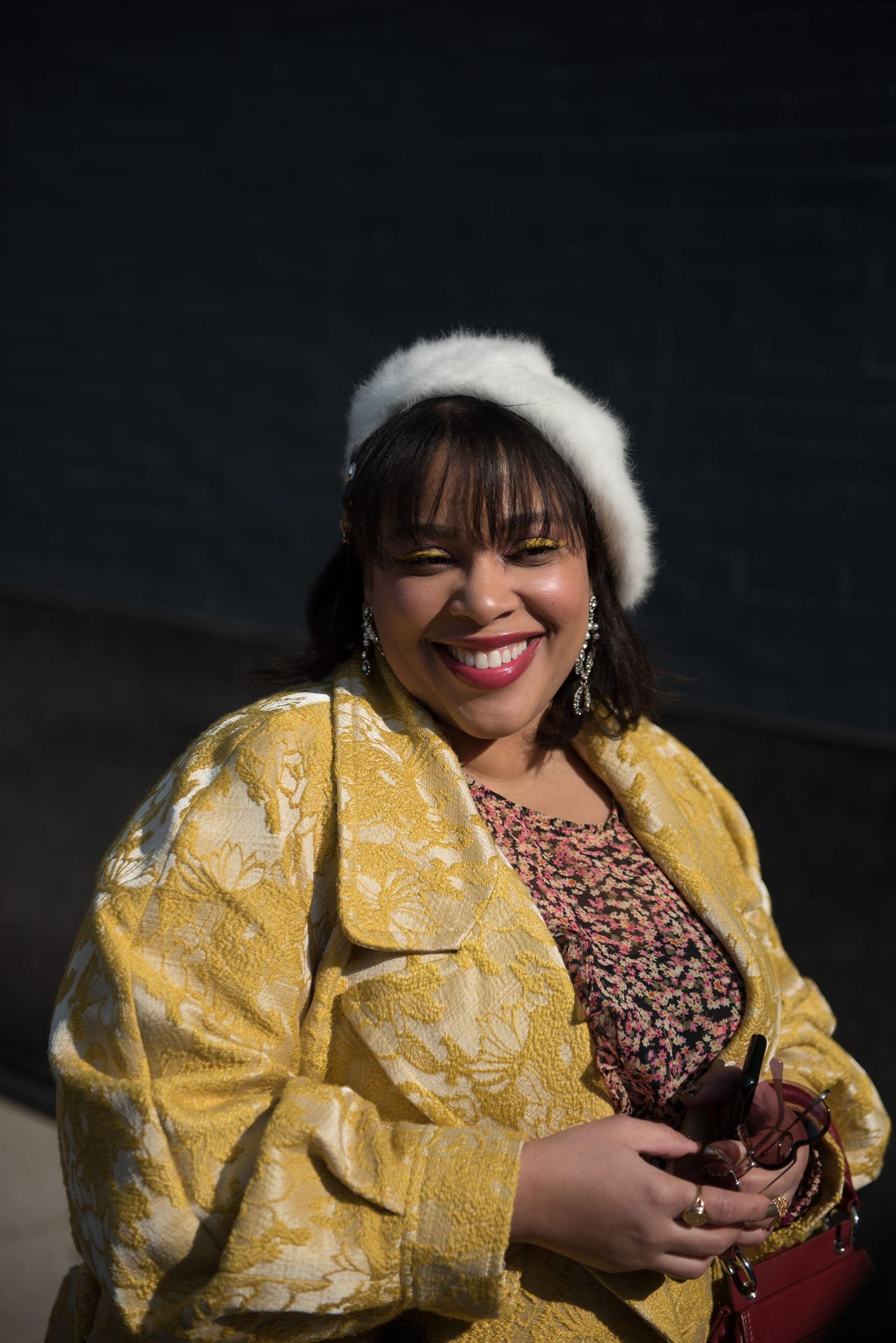 Femme souriante avec un bob brun foncé avec une frange, portant un béret blanc pelucheux.