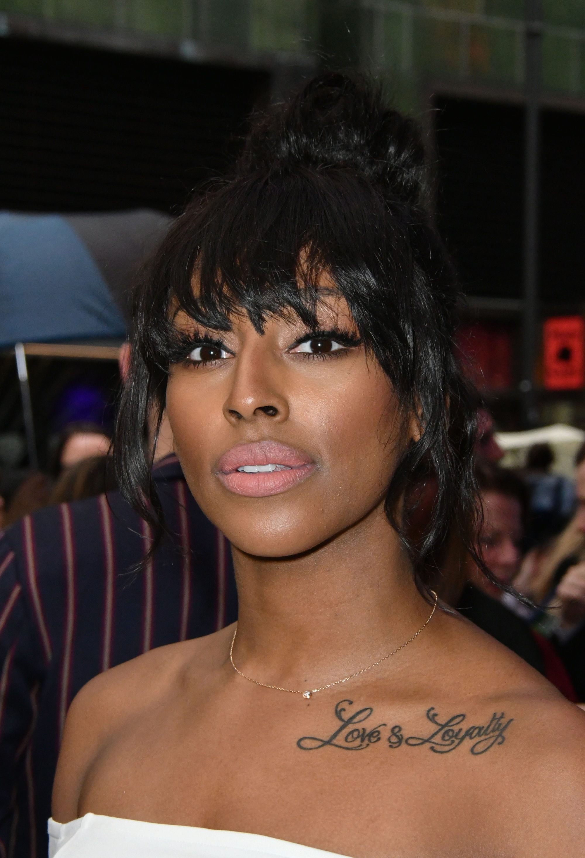 Alexandra Burke avec une frange rasant les sourcils et un chignon haut.