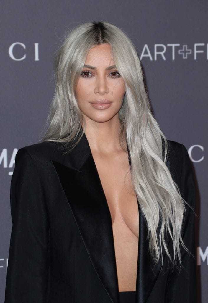 Nuances de cheveux blonds : Kim Kardashian West avec de très longs cheveux blonds argentés ondulés portant une robe blazer noire.