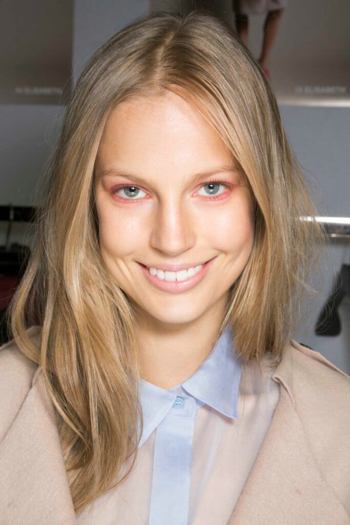 Nuances de cheveux blonds : Femme aux cheveux blonds raides et méchés, portant une chemise bleu clair avec une veste beige.