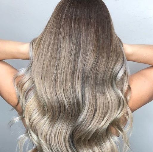 Nuances de cheveux blonds : Femme aux longs cheveux ondulés de blond cendré qui balaye ses cheveux en passant ses mains.