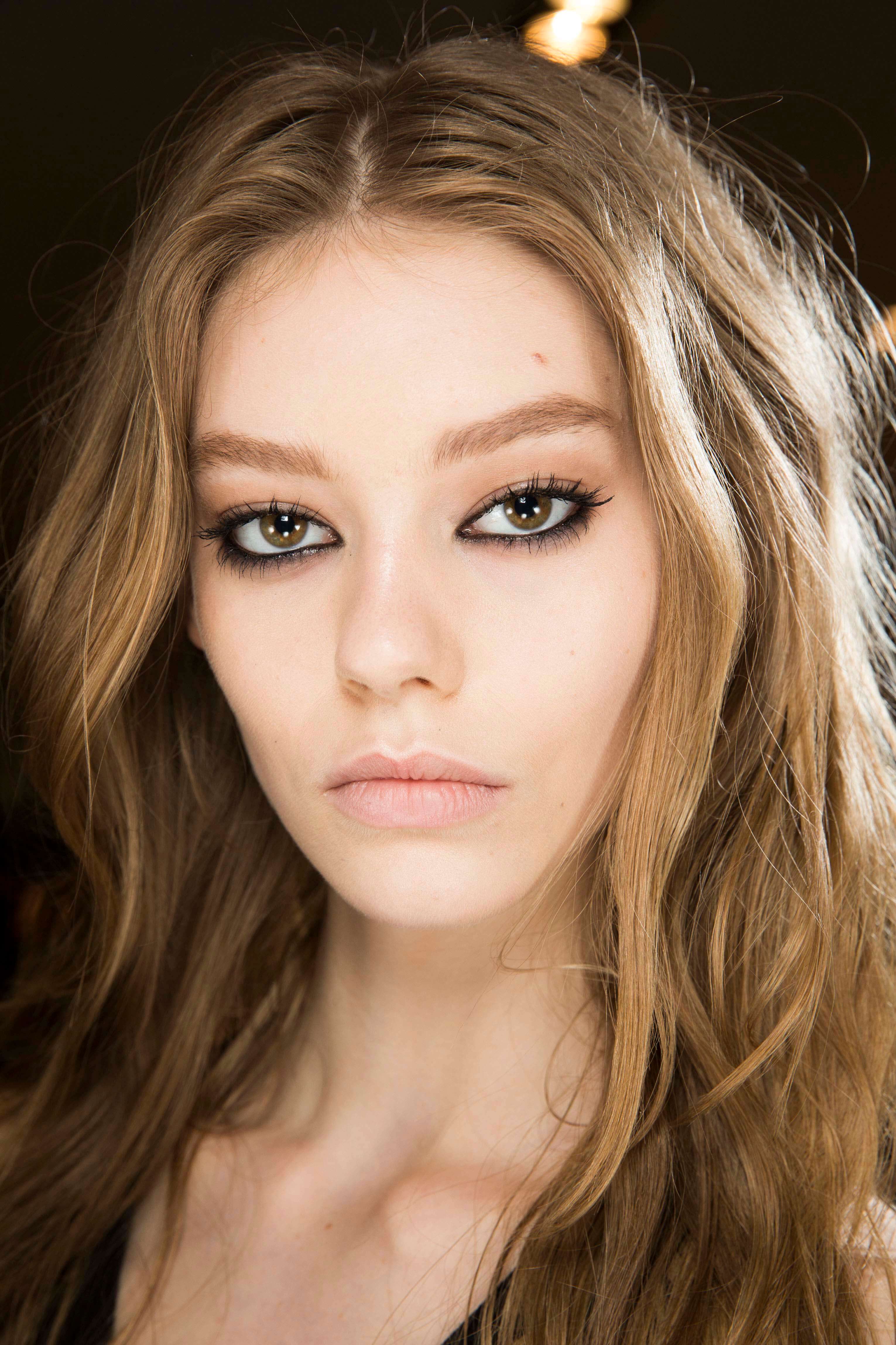 Nuances de cheveux blonds : Femme aux cheveux bruns ondulés d'un blond foncé et portant un maquillage épais pour les yeux.