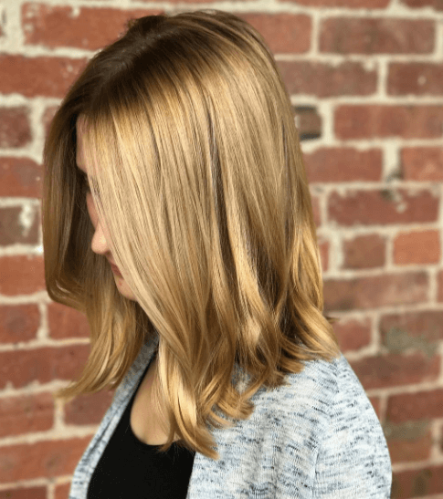 Nuances de cheveux blonds : Femme aux cheveux blonds caramélisés à longueur d'épaule avec une légère ondulation.