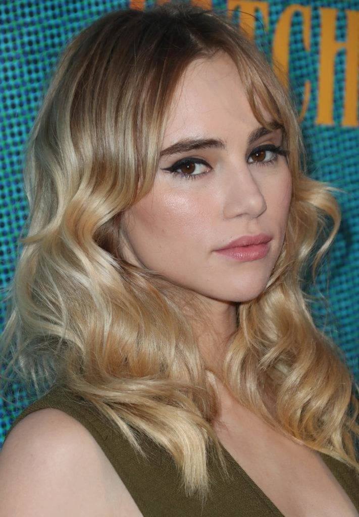 Nuances de cheveux blonds : Suki Waterhouse avec des cheveux blonds ondulés à balayage de longueur moyenne avec une longue frange centrale.