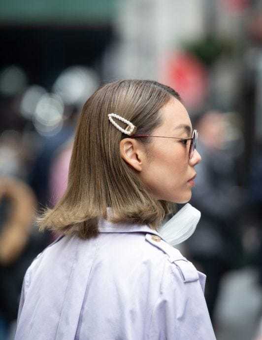 Nuances de cheveux blonds : Femme aux cheveux longs et raides de couleur cendre foncée, aux pointes redressées, portant un accessoire capillaire à clip et des lunettes de soleil.