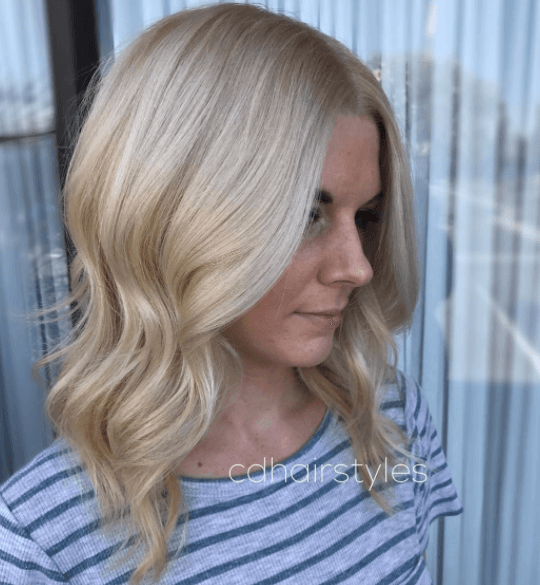 vue de côté d'une femme aux cheveux ondulés à longueur d'épaule et de couleur blonde