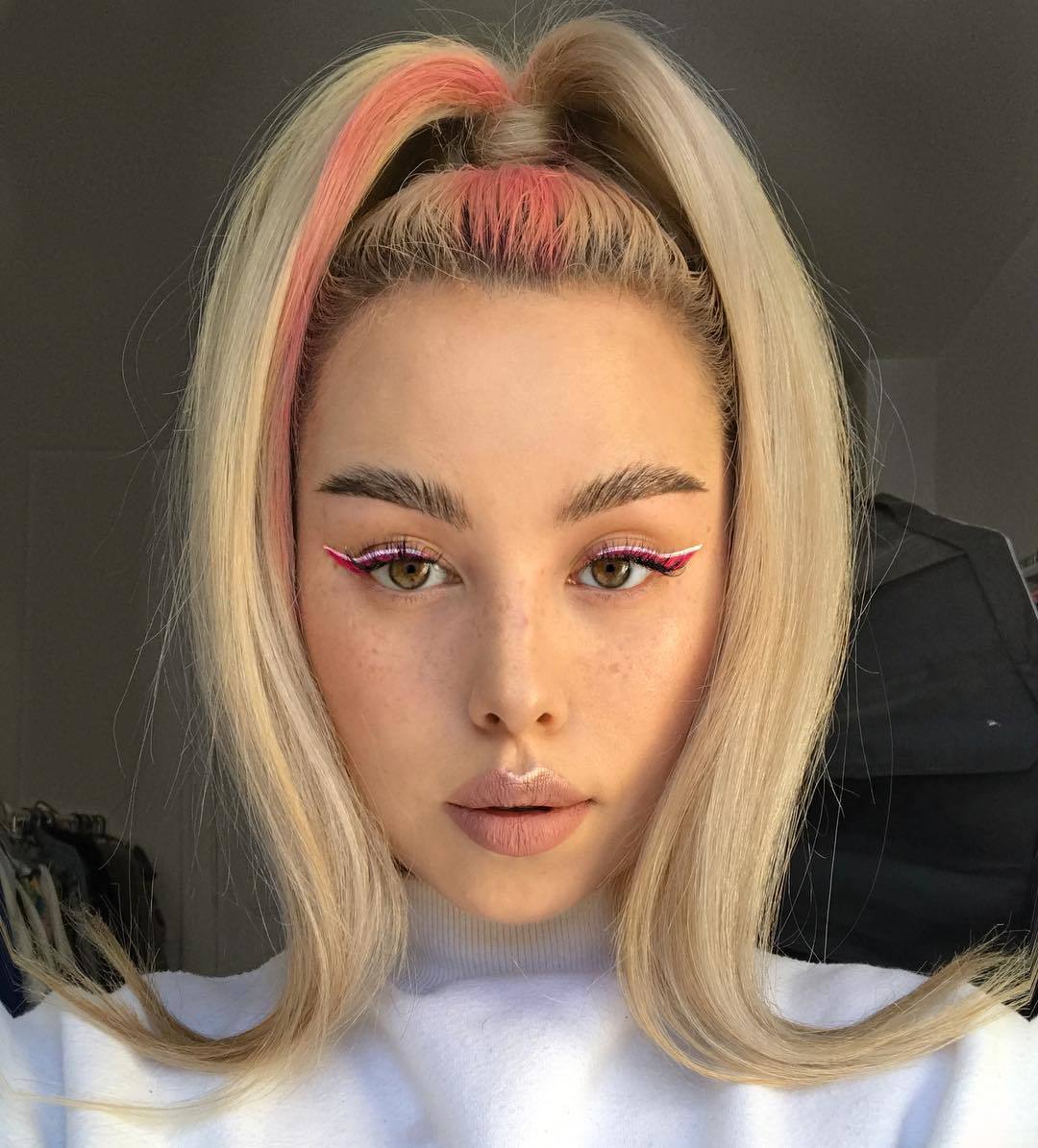 Femme aux cheveux blonds coiffée en poney haut avec une mèche de fille rose