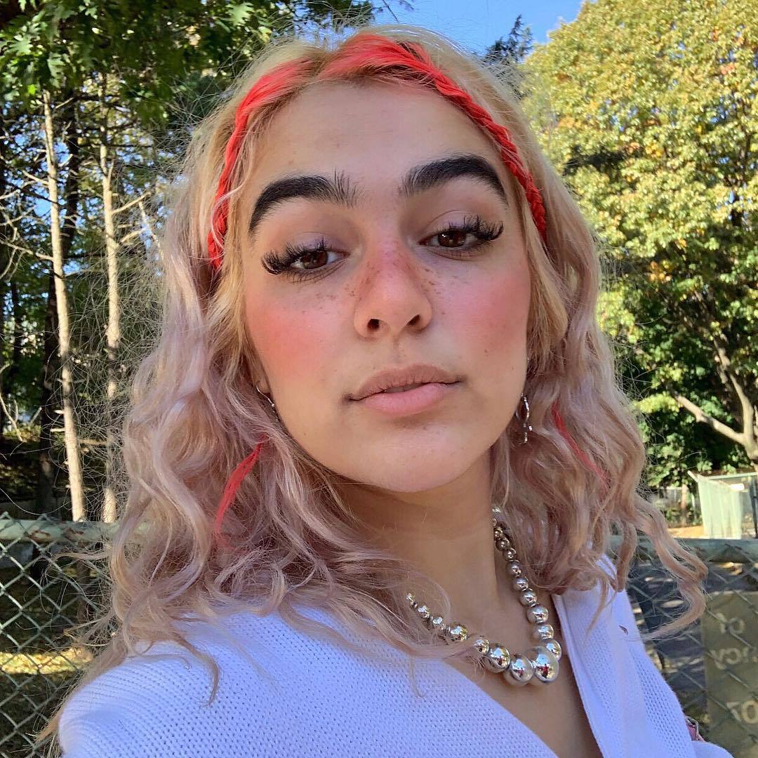 Femme aux cheveux blonds bouclés avec des mèches rouges tressées e girl