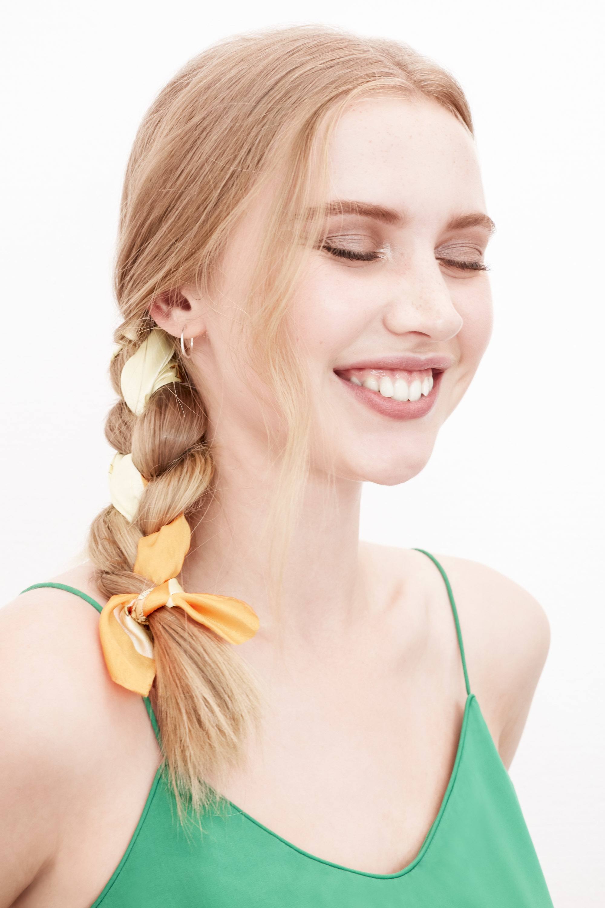 Des tresses faciles pour les cheveux longs : Photo d'une femme blonde avec une tresse de côté avec un ruban jaune, portant un cami top vert