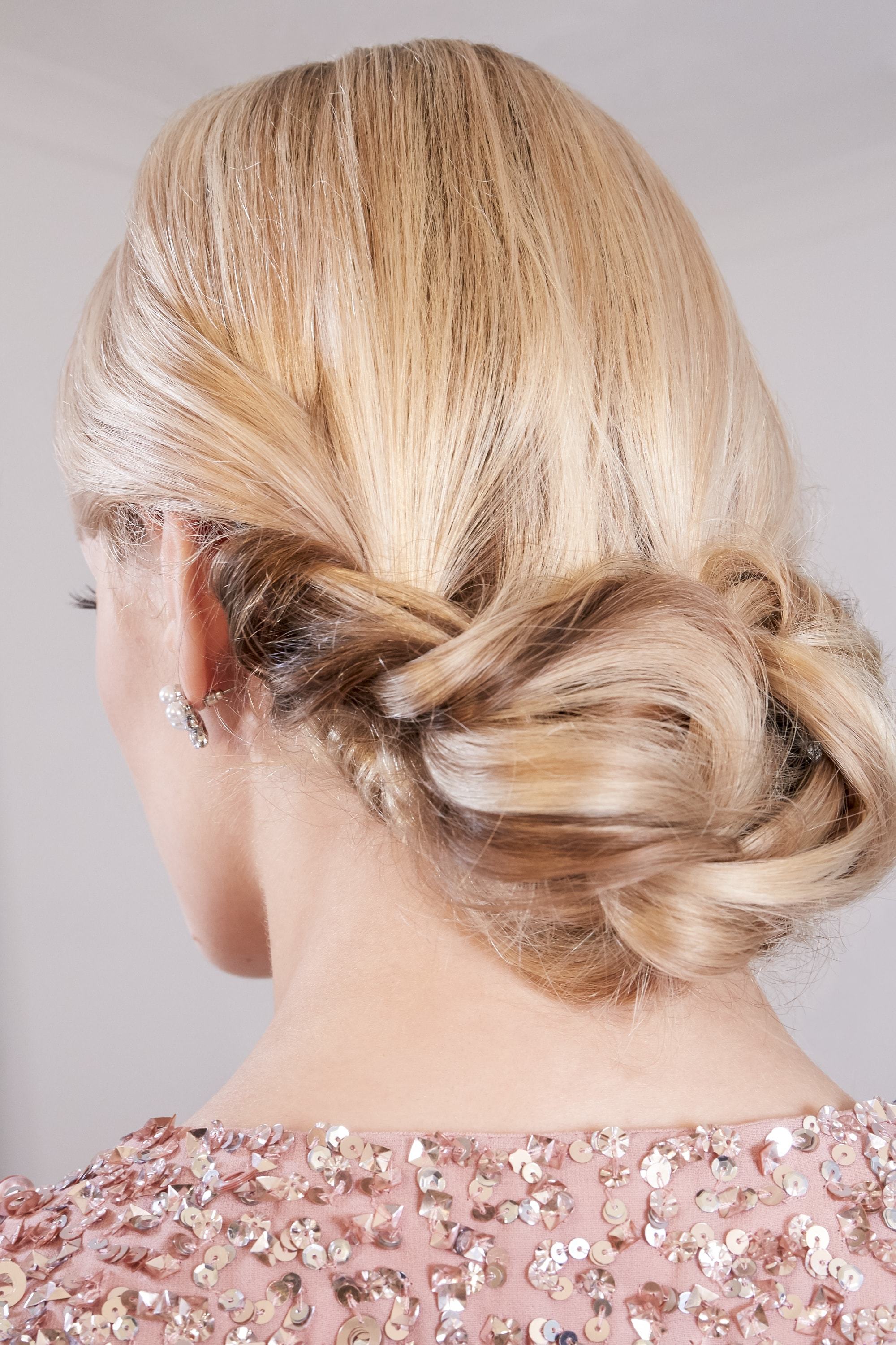 Des tresses faciles pour les cheveux longs : Vue de dos d'une femme blonde avec un chignon bas et tordu, portant une robe à paillettes roses
