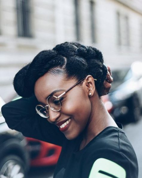 Coiffures d'hiver pour cheveux naturels : Femme souriante aux cheveux naturels foncés dans un style pompadour tordu, portant des lunettes et posant dans la rue
