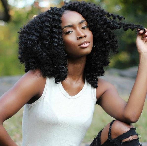 Coiffures d'hiver pour cheveux naturels : Femme avec des tresses en crochet brun foncé à la longueur des épaules, portant un haut de veste blanc et un jean noir déchiré aux genoux, posant à l'extérieur